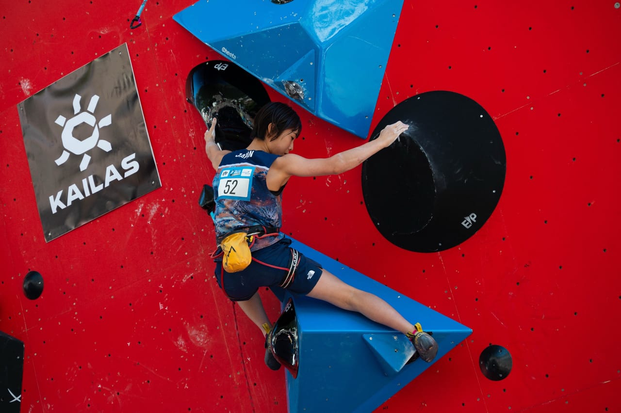 Japanese female climber reaching for a hold on the red lead wall